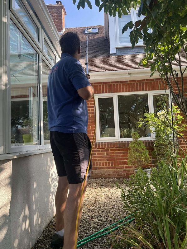 Jay cleaning the upstairs windows of a house using a water-fed pole